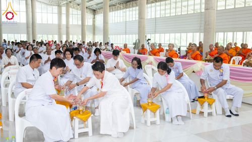 กลุ่มพุทธศาสนิกชนในชุดสีขาวกำลังประกอบพิธีกรรมทางศาสนาภายในอาคารโถงกว้าง