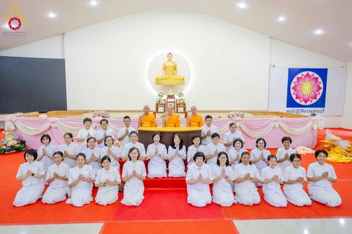กลุ่มพระภิกษุและผู้เข้าร่วมสัมมนาในชุดขาวนั่งเรียงแถวถ่ายภาพหมู่หน้าพระพุทธรูปภายในอาคารปฏิบัติธรรม