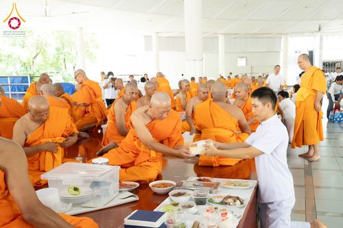 ชายชุดขาวกำลังประเคนอาหารให้พระภิกษุสงฆ์ในหอฉัน