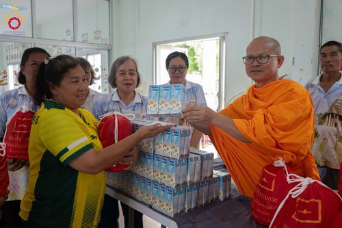 พระสงฆ์กำลังส่งมอบกล่องนมและถุงยังชีพสีแดงให้กับหญิงที่มารับความช่วยเหลือ