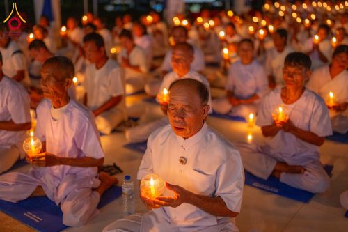 กลุ่มคนสวมชุดสีขาวนั่งถือเทียนในมือเพื่อประกอบพิธีกรรมทางศาสนาในตอนกลางคืน