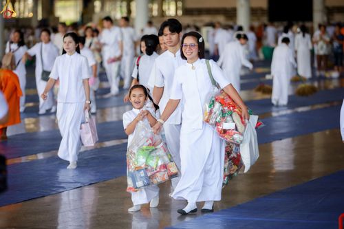 กลุ่มคนสวมชุดขาวถือถุงใส่ของทำบุญเดินอยู่ในอาคารโถงกว้าง