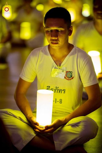 ชายหนุ่มสวมชุดสีขาวนั่งสมาธิถือโคมไฟส่องสว่างในห้องปฏิบัติธรรม