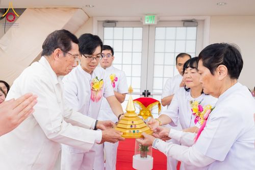 กลุ่มคนในชุดสีขาวกำลังประคองพานทองที่มีผอบทรงเจดีย์สีทองในพิธีทางศาสนา