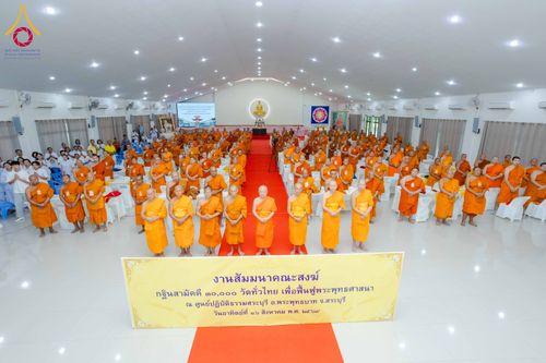 พระภิกษุสงฆ์และผู้เข้าร่วมงานสัมมนาโครงการกฐินสามัคคีจำนวนมากยืนรวมตัวกันภายในห้องประชุมขนาดใหญ่