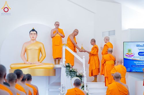 พระภิกษุสงฆ์ในจีวรสีส้มกำลังประกอบพิธีทางศาสนาหน้าพระพุทธรูปองค์สีทองภายในวัด