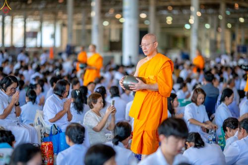 พระภิกษุสงฆ์เดินรับบิณฑบาตท่ามกลางพุทธศาสนิกชนชุดขาวในอาคารกว้าง