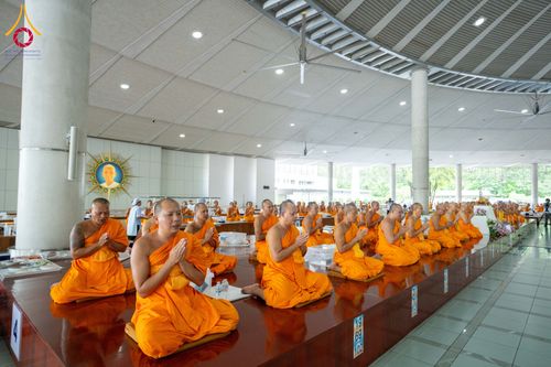 พระภิกษุสงฆ์หลายรูปนั่งพนมมือปฏิบัติธรรมบนพื้นยกระดับภายในอาคาร