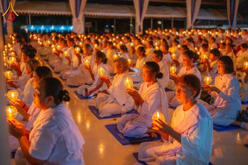 กลุ่มอุบาสิกาแก้วสวมชุดขาวนั่งเรียงแถวถือประทีปสว่างไสวในมือเพื่อทำพิธีจุดประทีป