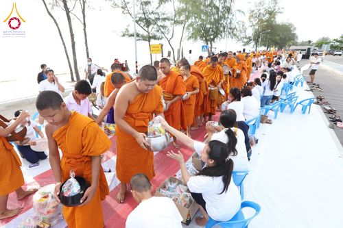 พระภิกษุสามเณรเดินรับบิณฑบาตจากประชาชนที่นั่งรอใส่บาตรริมชายหาด