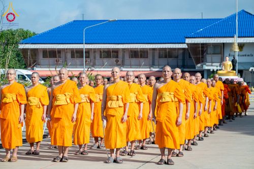 พระภิกษุสงฆ์จำนวนมากในจีวรสีเหลืองเดินเรียงแถวในพิธีทางศาสนาหน้าอาคาร