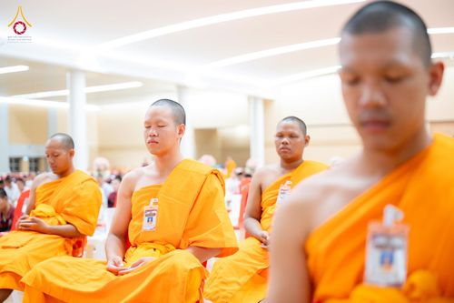 กลุ่มชายในชุดจีวรสีเหลืองทองนั่งหลับตาทำสมาธิภายในอาคาร