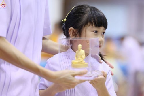 เด็กหญิงสวมชุดขาวถือกล่องใสบรรจุพระพุทธรูปองค์เล็กในงานพิธี