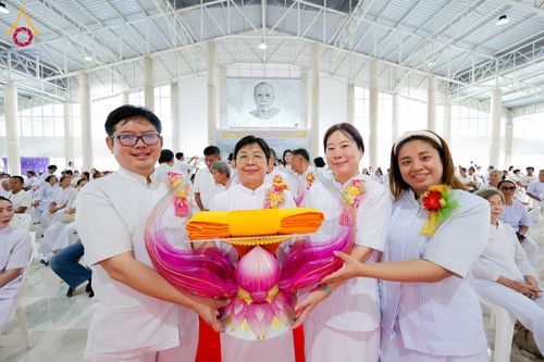 กลุ่มคนสี่คนสวมชุดสีขาวถือพานพุ่มวางผ้าไตรจีวรสีเหลืองในงานพิธีทางศาสนา