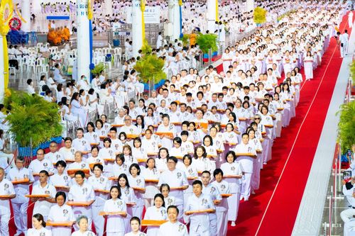 กลุ่มพุทธศาสนิกชนสวมชุดขาวถือพานผ้าป่าเดินแถวภายในอาคารขนาดใหญ่ที่มีพรมแดง