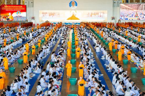 พุทธศาสนิกชนชุดขาวจำนวนมากนั่งเรียงแถวภายในสภาธรรมกายสากลเพื่อร่วมพิธีตักบาตรข้าวสารอาหารแห้งแด่พระภิกษุสงฆ์