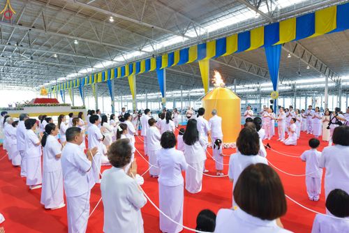 กลุ่มคนสวมชุดขาวถือสายสิญจน์ร่วมพิธีจุดเทียนใจ ไฟนิรันดร์ อนันตชัย ภายในอาคาร
