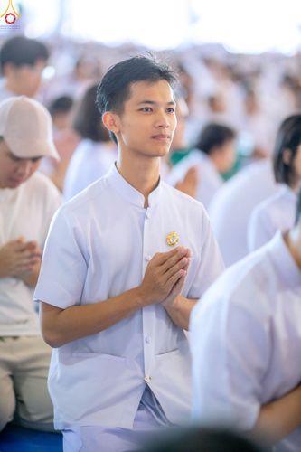 ชายหนุ่มสวมชุดสีขาวพนมมือด้วยความสงบในพิธีทางศาสนาที่มีผู้คนเข้าร่วมจำนวนมาก