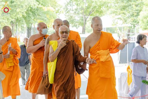กลุ่มพระภิกษุสงฆ์หลายรูปกำลังเดินสนทนากันในพื้นที่จัดงานสัมมนาท่ามกลางบรรยากาศร่มรื่น