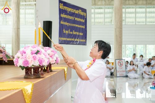 หญิงสวมชุดขาวกำลังจุดเทียนบูชาหน้าโต๊ะหมู่บูชาที่มีพานดอกไม้ประดับ