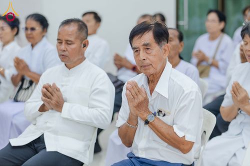 กลุ่มพุทธศาสนิกชนชายหญิงสวมชุดสีขาวนั่งพนมมือด้วยความสงบเรียบร้อยภายในอาคาร