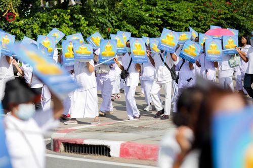 กลุ่มคนสวมชุดขาวเดินถือป้ายภาพพระประธานในขบวนพิธีทางศาสนา