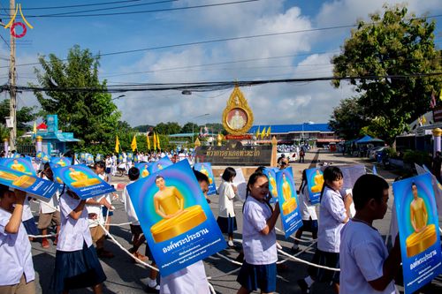 กลุ่มนักเรียนถือป้ายภาพพระพุทธรูปเดินขบวนในงานพิธี