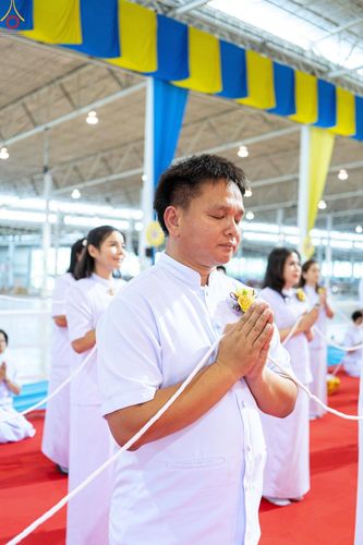ชายและหญิงสวมชุดขาวกำลังพนมมือประกอบพิธีทางศาสนาภายในอาคาร