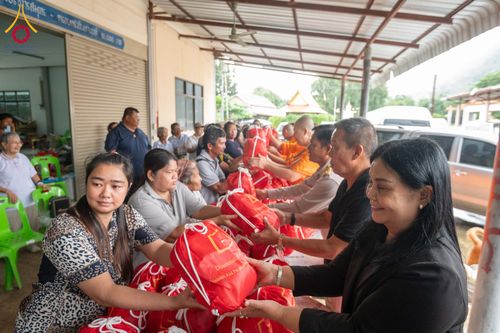 กลุ่มคนและพระภิกษุกำลังส่งมอบถุงยังชีพสีแดงให้แก่ประชาชนในพื้นที่ประสบภัย