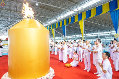 กลุ่มคนในชุดขาวกำลังประกอบพิธีจุดเทียนใจ ไฟนิรันดร์ อนันตชัย โดยมีโคมไฟสีทองขนาดใหญ่อยู่ด้านหน้า