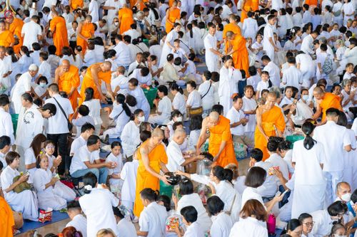 พุทธศาสนิกชนสวมชุดขาวกำลังตักบาตรข้าวสารอาหารแห้งแด่พระภิกษุสงฆ์ในอาคารขนาดใหญ่