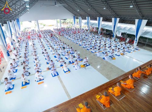 กลุ่มผู้เข้าร่วมโครงการอบรมสวมชุดขาวนั่งปฏิบัติธรรมภายในอาคารกว้างขวาง โดยมีพระภิกษุสงฆ์นั่งอยู่ด้านหน้า