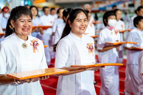 หญิงไทยสองคนยิ้มแย้มสวมชุดสีขาวถือผ้าสีเหลืองในพิธีทางศาสนา