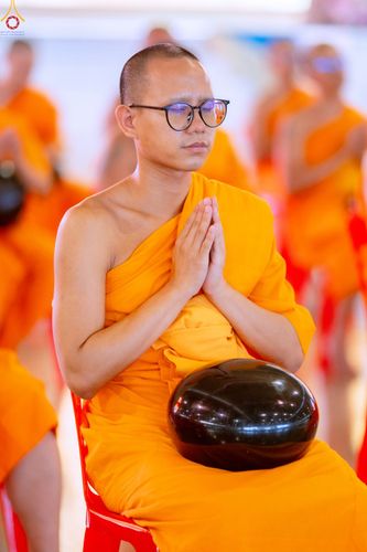 พระภิกษุสงฆ์สวมแว่นตานั่งประนมมือถือบาตรในพิธีตักบาตร