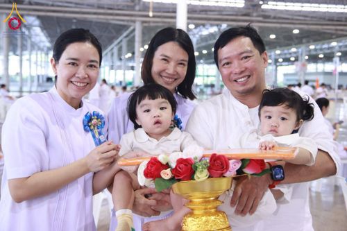 ครอบครัวสวมชุดสีขาวอุ้มเด็กเล็กสองคนร่วมพิธีทอดผ้าป่าในอาคารสภาธรรมกายสากล