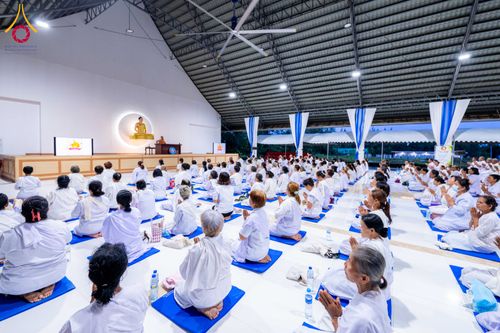 ผู้เข้าร่วมโครงการอบรมในชุดสีขาวนั่งเรียงแถวบนเบาะรองนั่งภายในอาคารเพื่อปฏิบัติธรรม