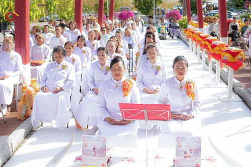 กลุ่มคนสวมชุดขาวนั่งพนมมือในพิธีทางศาสนาพุทธกลางแจ้ง