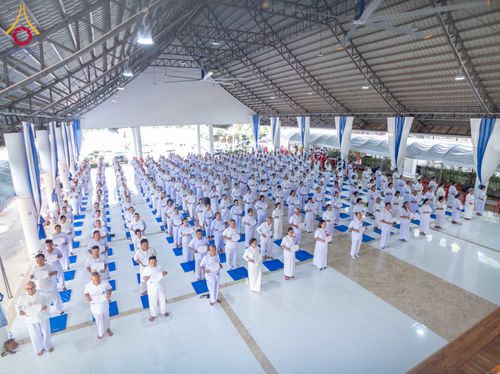 กลุ่มผู้เข้าร่วมโครงการอบรมสวมชุดขาวจำนวนมากยืนเรียงแถวอย่างเป็นระเบียบภายในอาคารปฏิบัติธรรม