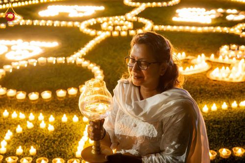 หญิงสวมชุดสีขาวถือโคมประทีปท่ามกลางการจุดประทีปจำนวนมากบนพื้นหญ้าในยามค่ำคืน