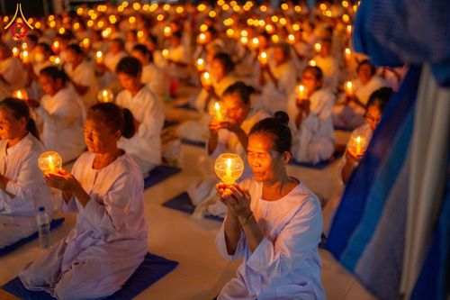 กลุ่มอุบาสิกาชุดขาวถือประทีปในมือขณะนั่งสมาธิในพิธีจุดประทีป