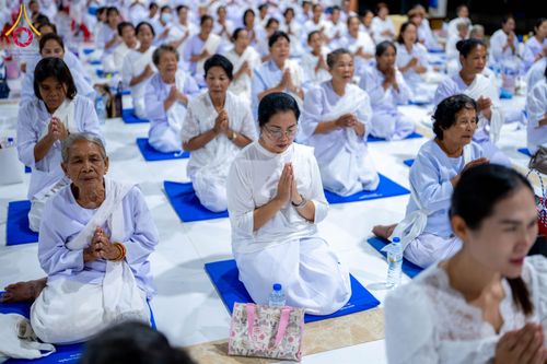 กลุ่มอุบาสิกาแก้วสวมชุดสีขาวนั่งพนมมือปฏิบัติธรรมบนเบาะรองนั่งภายในอาคาร