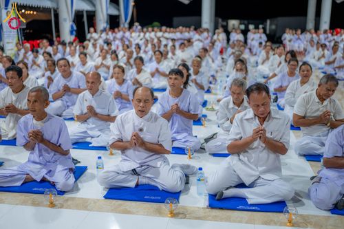 กลุ่มอุบาสกและอุบาสิกาสวมชุดขาวนั่งพนมมือปฏิบัติธรรมบนเบาะรองนั่งภายในอาคาร