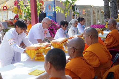 กลุ่มสาธุชนในชุดขาวกำลังถวายผ้าไตรแด่พระภิกษุสงฆ์ในพิธีทางศาสนา