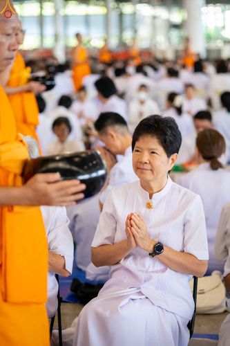 หญิงสวมชุดขาวพนมมือรับบิณฑบาตจากพระภิกษุในพิธีทำบุญ