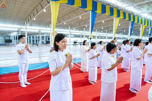 กลุ่มคนสวมชุดขาวพนมมือถือสายสิญจน์ในพิธีทางศาสนาภายในอาคาร