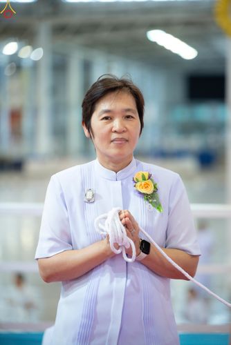 หญิงวัยกลางคนสวมชุดสีขาวถือสายสิญจน์ในมือขณะประกอบพิธีกรรม