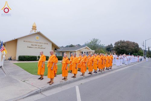 พระภิกษุสงฆ์และพุทธศาสนิกชนเดินแถวเรียงกันบนทางเท้าหน้าอาคารวัดพระธรรมกายซิลิคอนวัลเลย์