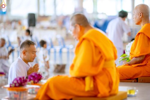 ชายสวมชุดขาวนั่งพนมมือไหว้พระภิกษุสงฆ์ในพิธีทางศาสนา