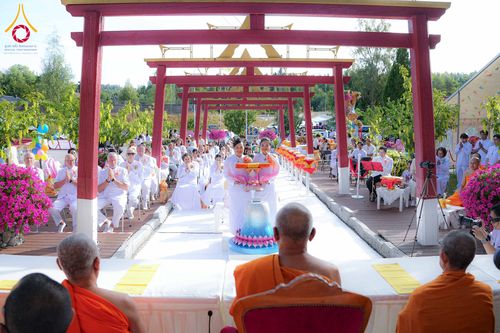 พุทธศาสนิกชนชุดขาวร่วมพิธีทอดผ้าป่าสามัคคีภายใต้ซุ้มประตูสีแดง โดยมีพระภิกษุสงฆ์เป็นประธานในพิธี