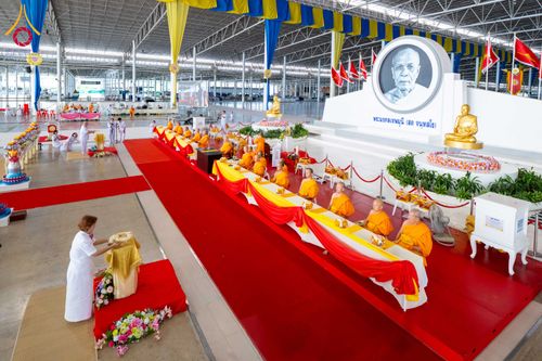พระภิกษุสงฆ์นั่งเรียงแถวบนอาสนะเพื่อรับถวายมหาสังฆทานภายในอาคารขนาดใหญ่ที่มีพุทธศาสนิกชนชุดขาวร่วมพิธี